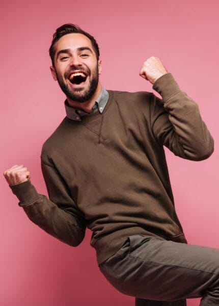 Happy man celebrates victory and smiles on pink background